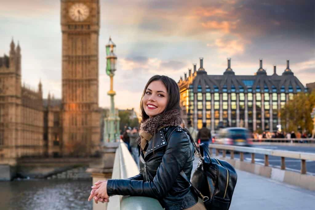 portrait smiling young woman standing against tower bridge city sunset