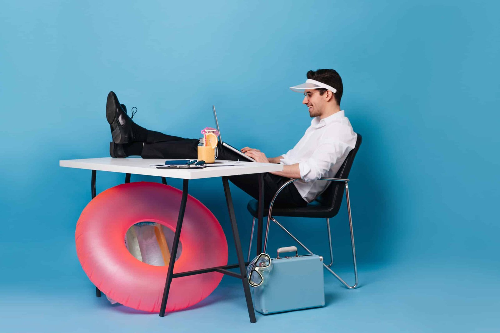 guy cap works with laptop sitting with his legs thrown table portrait man against space suitcase inflatable circle scaled